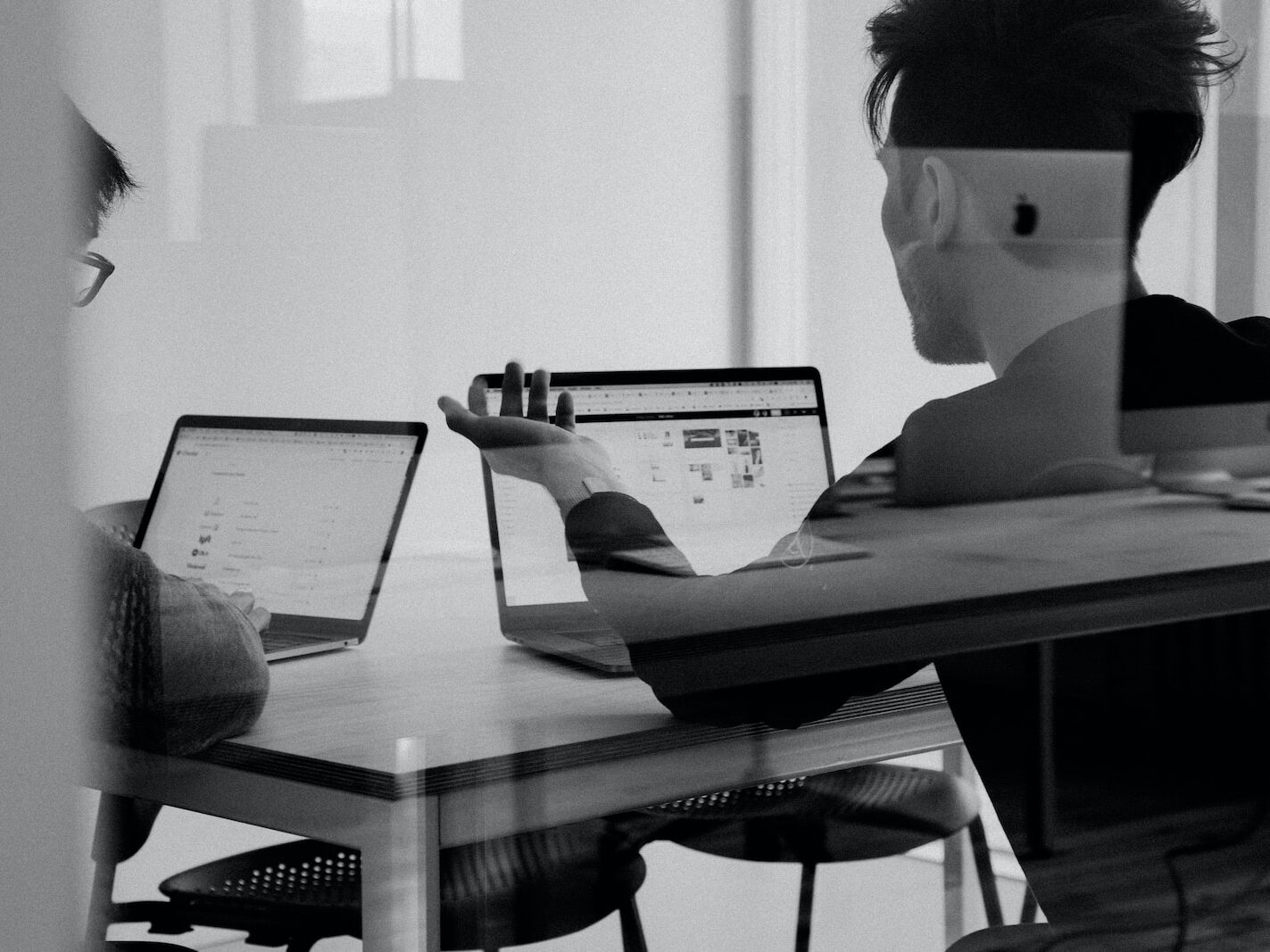 man using MacBook having a discussion with another person using. a macbook